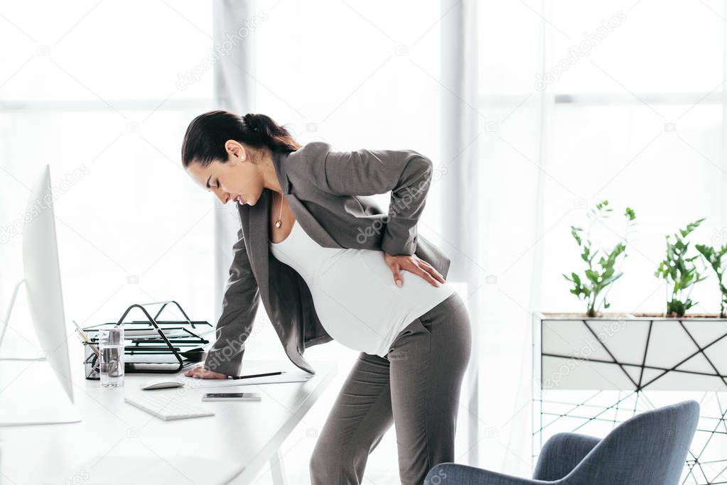 pregnant woman enduring pain and leaning on table 