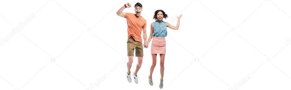 panoramic shot of happy man and woman holding hands and jumping while showing triumph gestures isolated on white