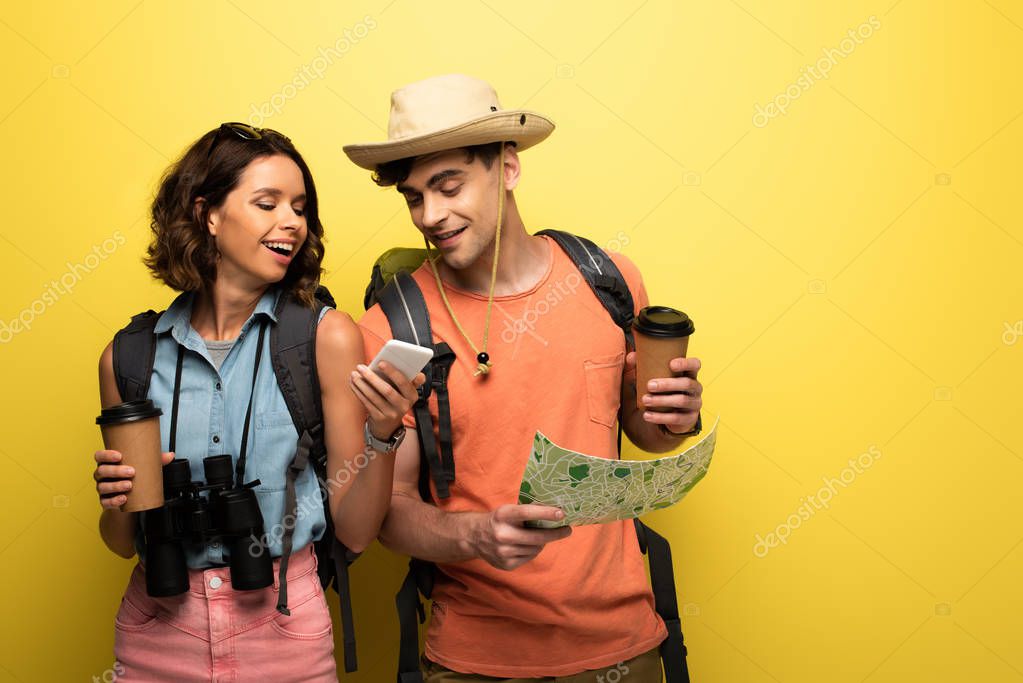 cheerful woman showing smartphone to man with geographic map on yellow background