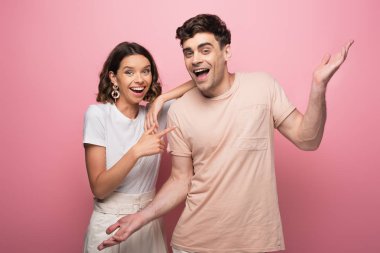 pembe arka plan üzerinde güzel kız arkadaşı yakınında dururken silkme jest gösteren neşeli genç adam