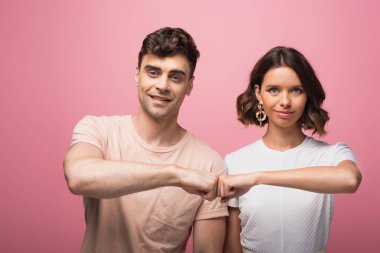 pembe arka planda kameraya bakarken neşeli erkek ve kadın yumruk yumruğa yapıyor