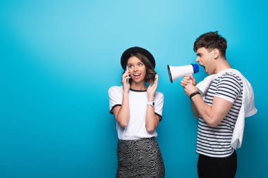 irritated man quarreling in loudspeaker at girlfriend talking on smartphone on blue background clipart