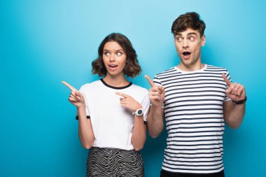 positive man and woman looking away and pointing with fingers on blue background