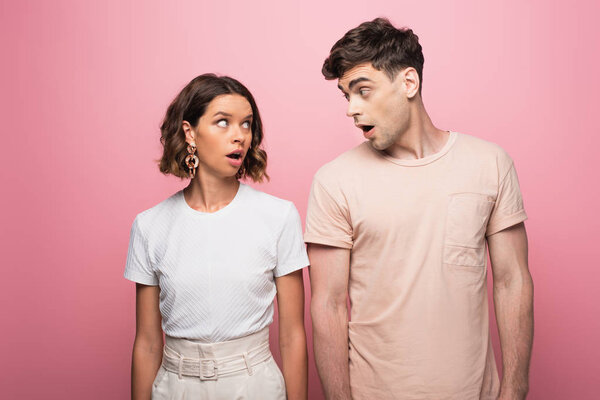 young couple quarreling while looking at each other on pink background