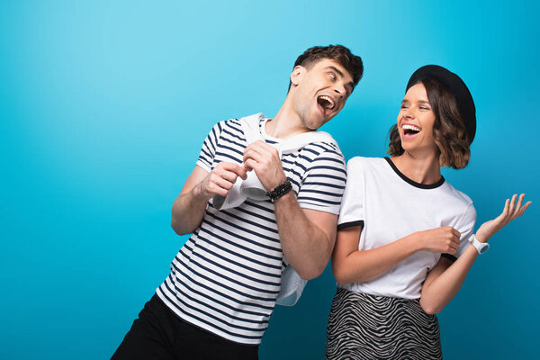 trendy, excited man and woman laughing together on blue background