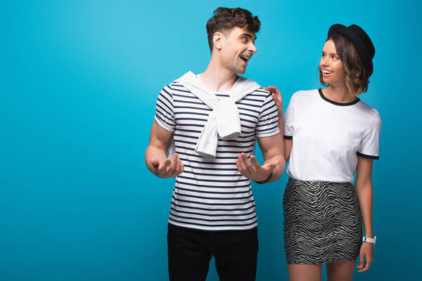 excited young man talking to smiling girlfriend on blue background