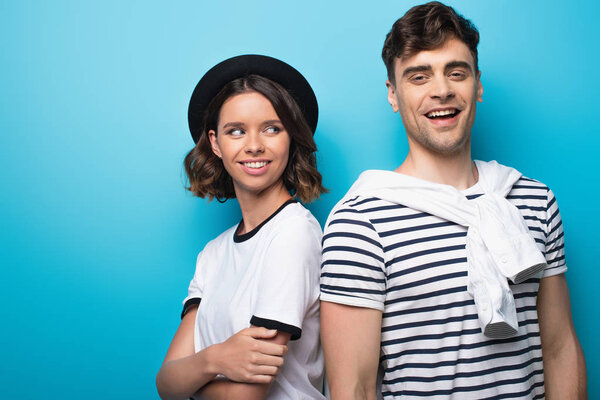 cheerful young woman standing near smiling boyfriend on blue background