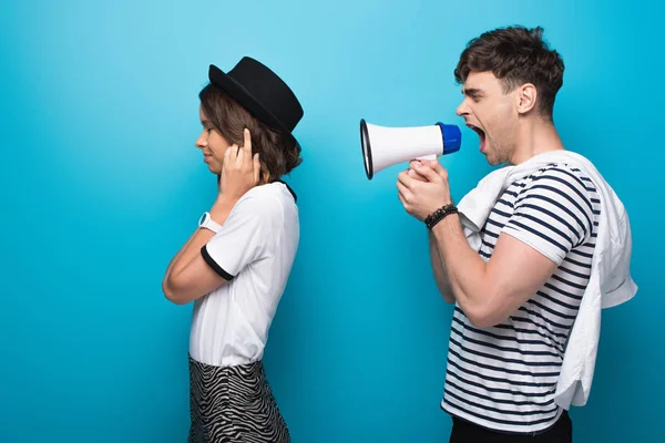 Angry Man Quarreling Loudspeaker Girlfriend Plugging Ears Fingers Blue Background — Stock Photo, Image