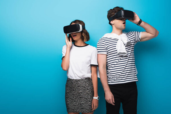 young, trendy man and woman using virtual reality headsets on blue background