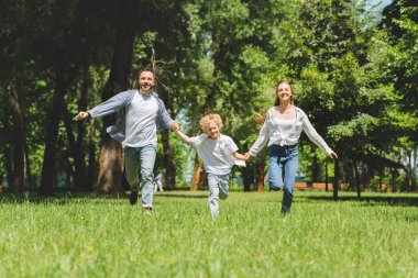 heyecanlı aile el ele tutuşuyor ve gündüz parkta koşuyor