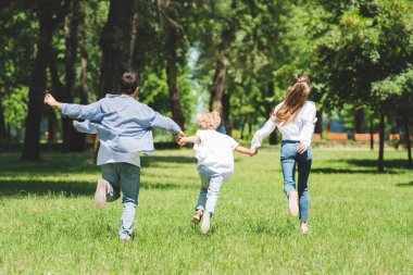 happy family holding hands and running in park during daytime clipart