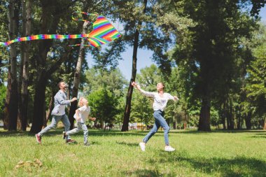 happy family running and playing with colorful flying kite in park clipart