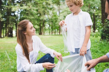 baba, anne ve oğlu gündüz parkta plastik torbalarda çöp toplama