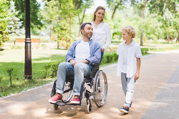 mother and adorable son with disabled father on wheelchair in park