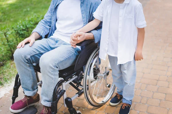Visão Cortada Filho Hloding Mãos Com Pai Deficiente Cadeira Rodas — Fotografia de Stock