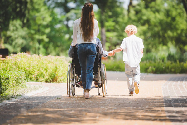 back view of mother and son with disabled father on wheelchair in park