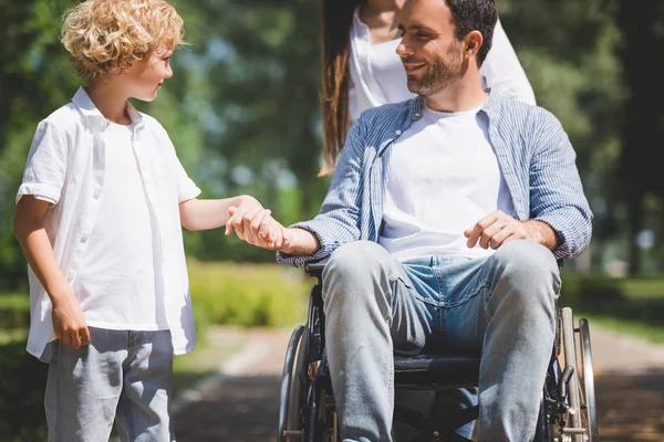 Son Hålla Händerna Med Handikappade Fader Rullstol Parken — Stockfoto