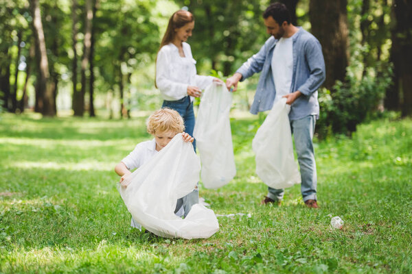 семья собирает мусор в пластиковых пакетах в парке
