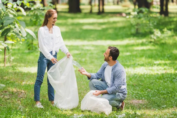 man and woman picking up garbage in plastic bags in park