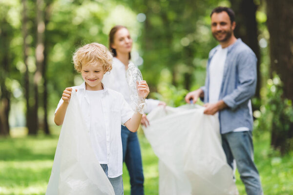 happy family picking up garbage in plastic bags in park