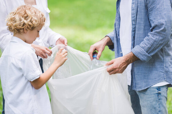 cropped view of family picking up garbage in plastic bag in park