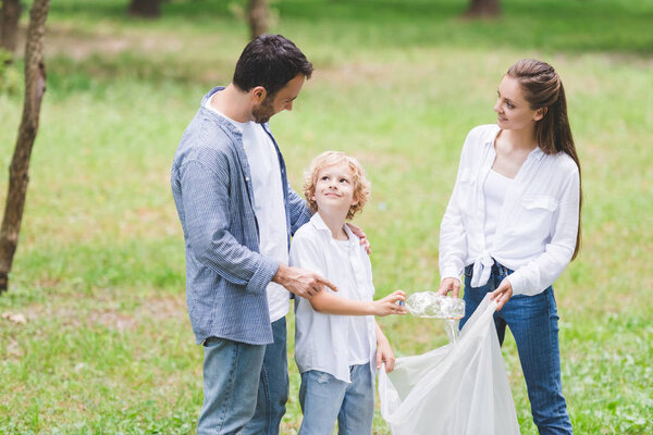 family in casual clothes picking up garbage in plastic bag in park