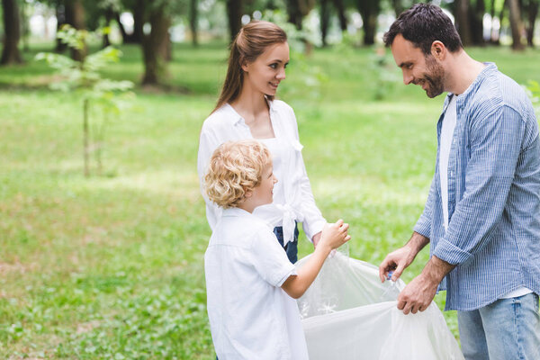family picking up garbage in plastic bags in park with copy space
