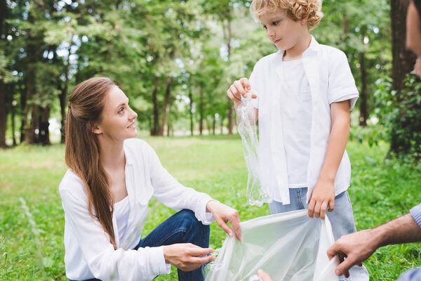 father, mother and son picking up garbage in plastic bags in park during daytime