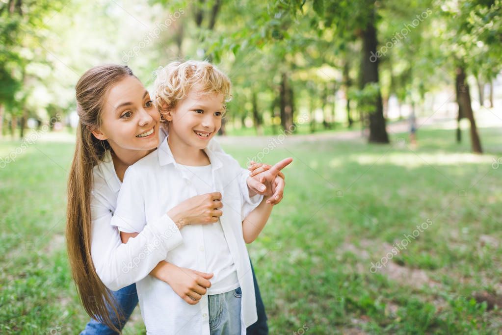 beautiful mother hugging adorable son pointing with finger at copy space in park