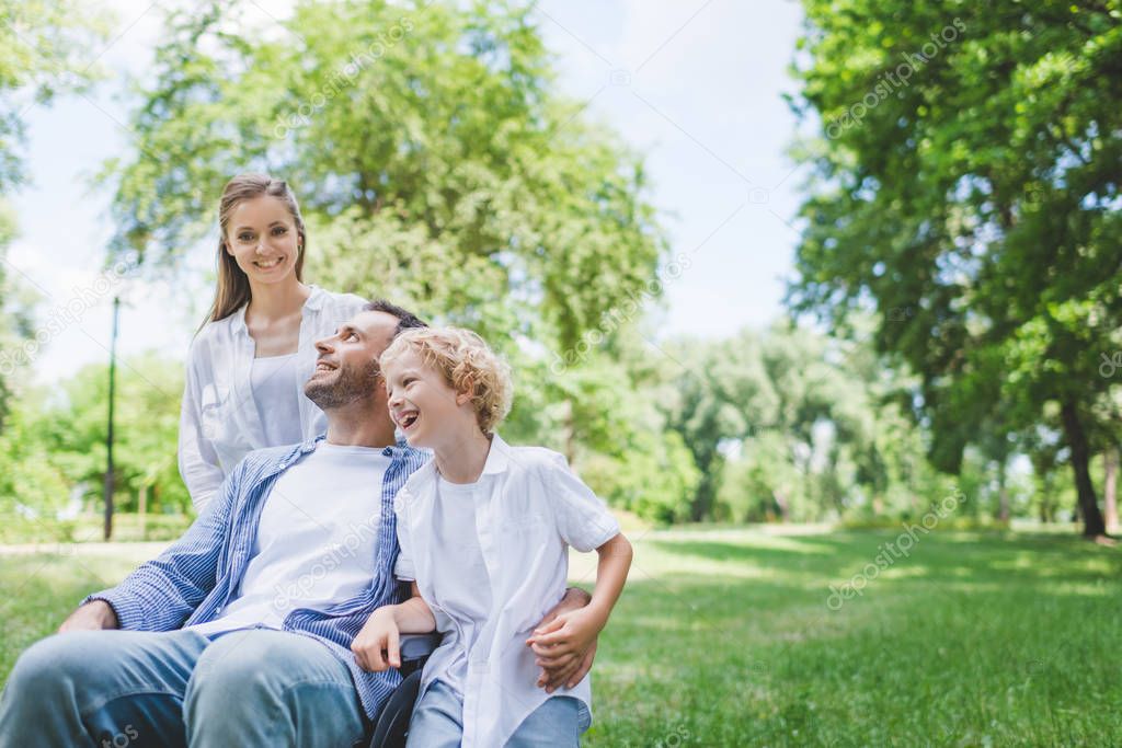 happy mother and son with disabled father on wheelchair in park