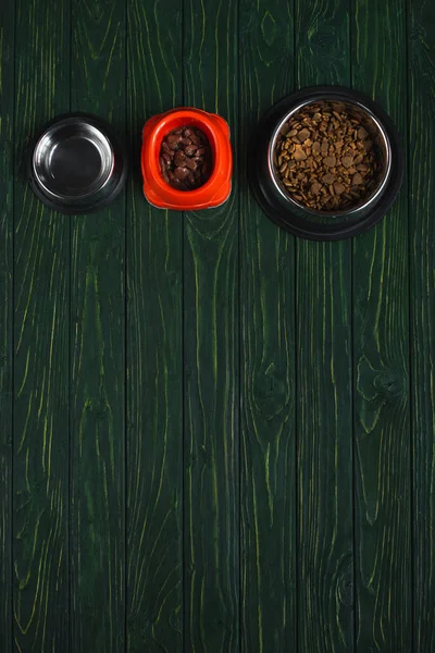 在绿色的木制表面上 一排带宠物食品的碗顶视图 带有复制空间 — 图库照片