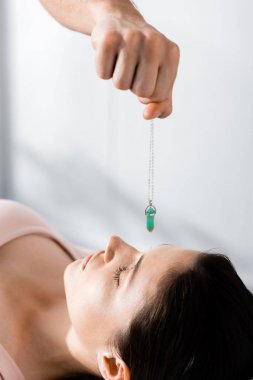 cropped view of hypnotist standing near woman and holding green stone above her face clipart