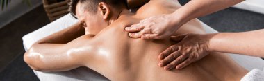panoramic shot of masseur and shirtless man lying on massage table clipart