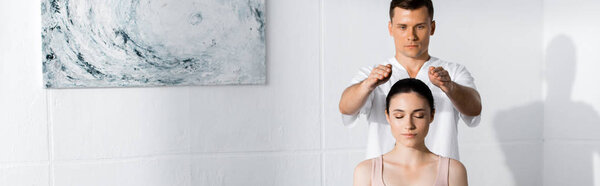 Панорамный снимок молодой женщины, сидящей с закрытыми глазами, пока целительница чистит свою ауру
