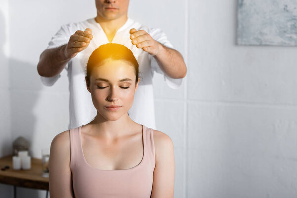 обрезанный вид целителя, стоящего рядом с женщиной с закрытыми глазами и держащего руки над головой
