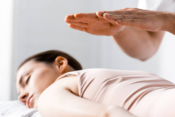 обрезанный вид целителя, стоящего рядом с женщиной, лежащей с закрытыми глазами и держащей руки над телом
