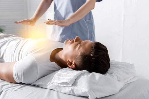 partial view of healer standing near man on massage table and holding hands above his body