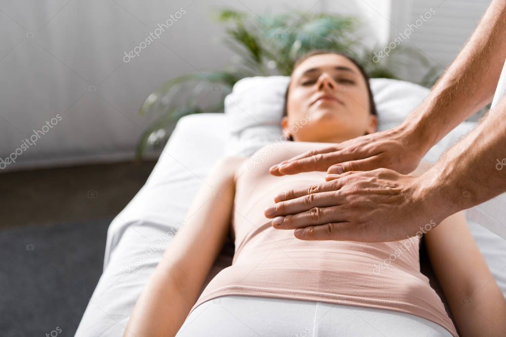 cropped view of healer standing near woman and holding hands above her stomach