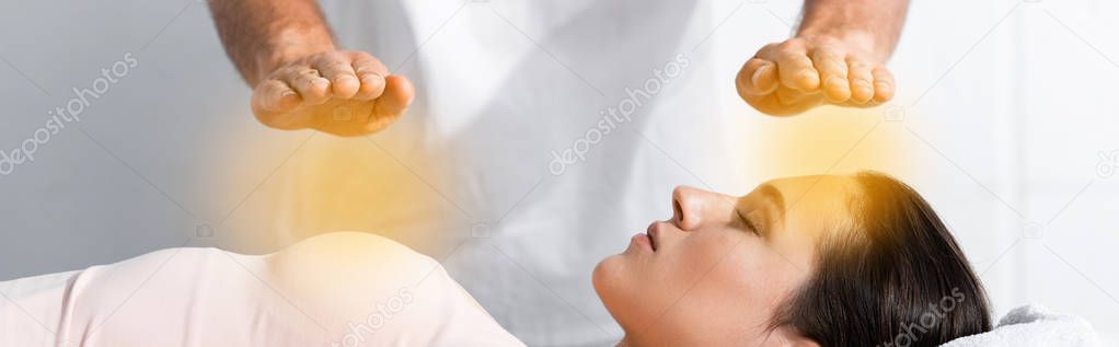 panoramic shot of healer standing near woman with closed eyes and holding hands above her body