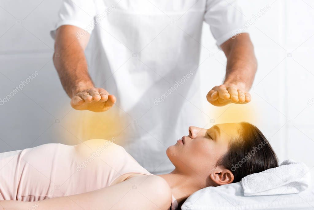 cropped view of healer standing near woman with closed eyes and holding hands above her body