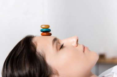 woman lying with closed eyes with colorful stones on forehead clipart