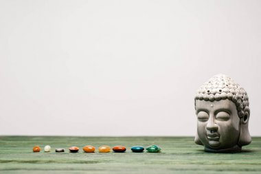 buddha statuette and colorful semiprecious stones on wooden surface isolated on grey clipart