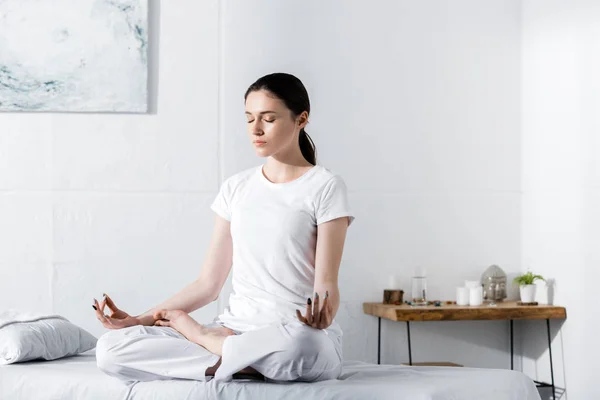 young woman sitting in lotus pose with closed eyes on massage table