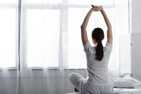 back view of woman with ponytail sitting on bed and stretching in clinic