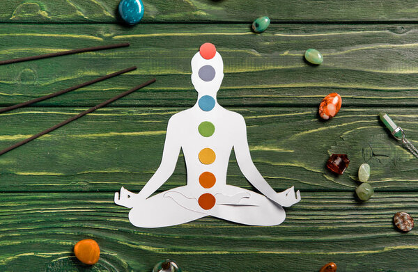 top view of paper figure in form of person with chakras in lotus pose, aroma sticks and colorful stones on wooden surface
