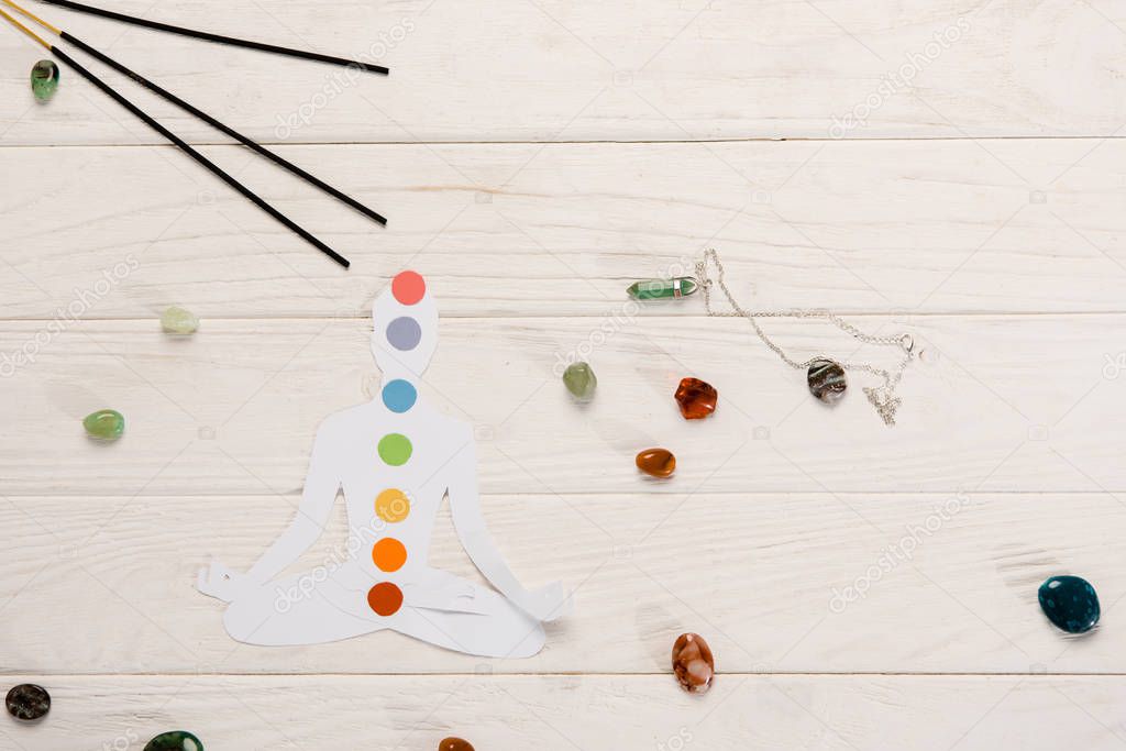 top view of paper figure in form of person with chakras in lotus pose, aroma sticks and colorful stones on wooden surface