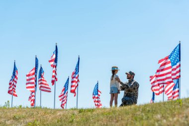Askeri üniformalı babanın seçici odak Amerikan bayrakları yakınındaki kızı bakarak 