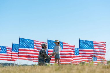 Amerikan bayrakları yakınında sevimli çocuk ile el ele tutuşan askeri baba seçici odak 