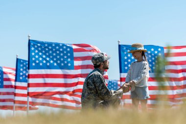 Amerikan bayrakları yakınında neşeli çocuk ile el ele tutuşan askeri baba seçici odak 