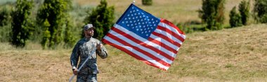 panoramic shot of handsome military man in uniform and cap holding american flag  clipart